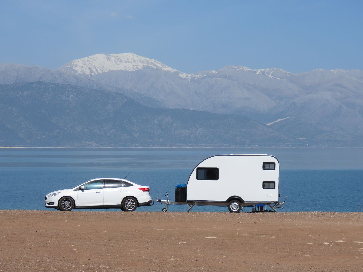 Auto en caravan aan het meer van Eğirdir, met bergen op de achtergrond.